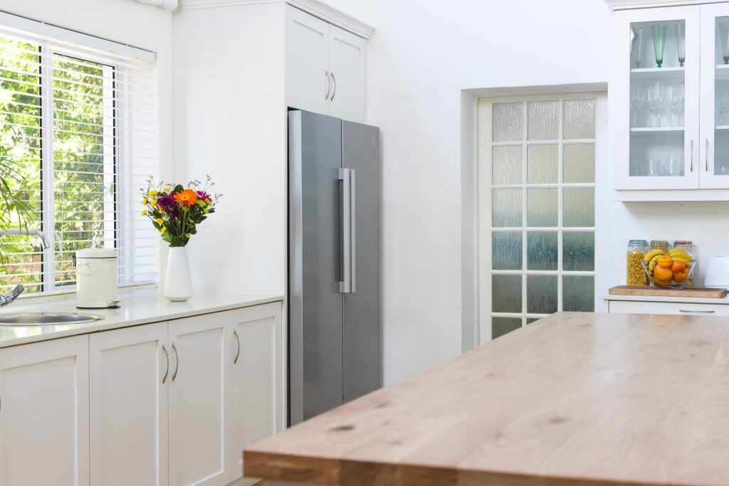 A tall stainless refrigerator column standing in a white cabinetry niche beside a glazed door