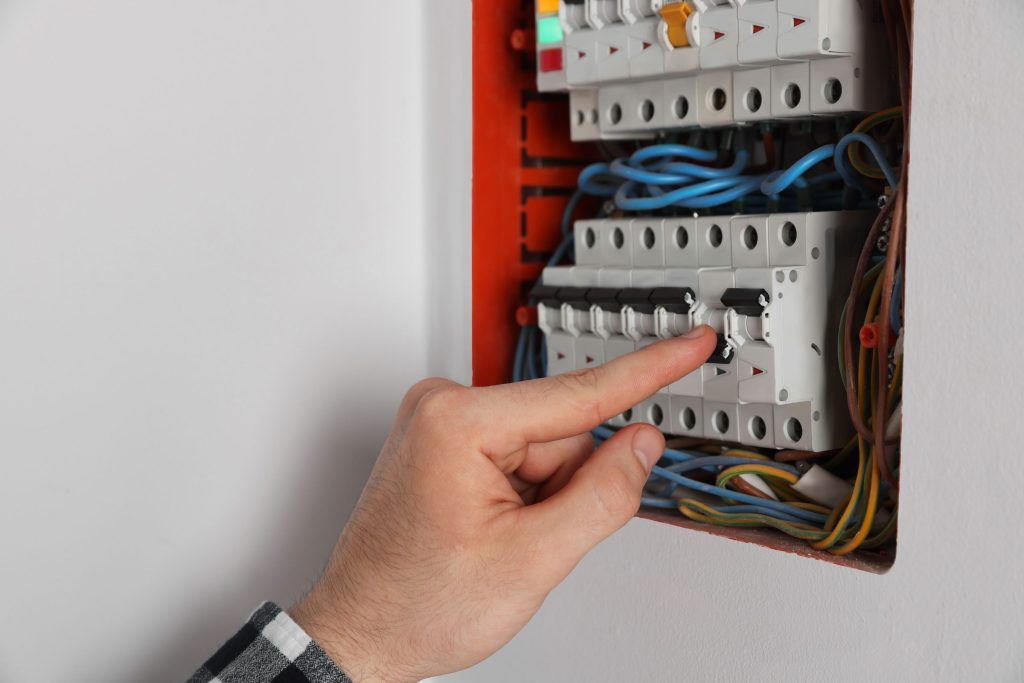 A hand switching a breaker in an open household panel.