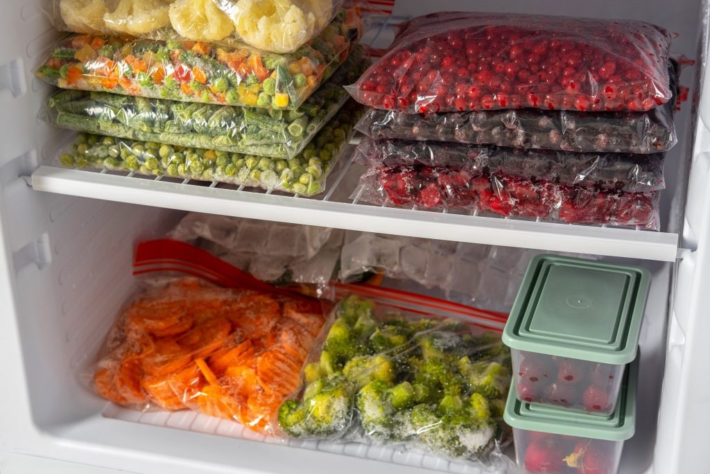 Bags and boxes of frozen vegetables and berries stacked on the shelves of a freezer.
