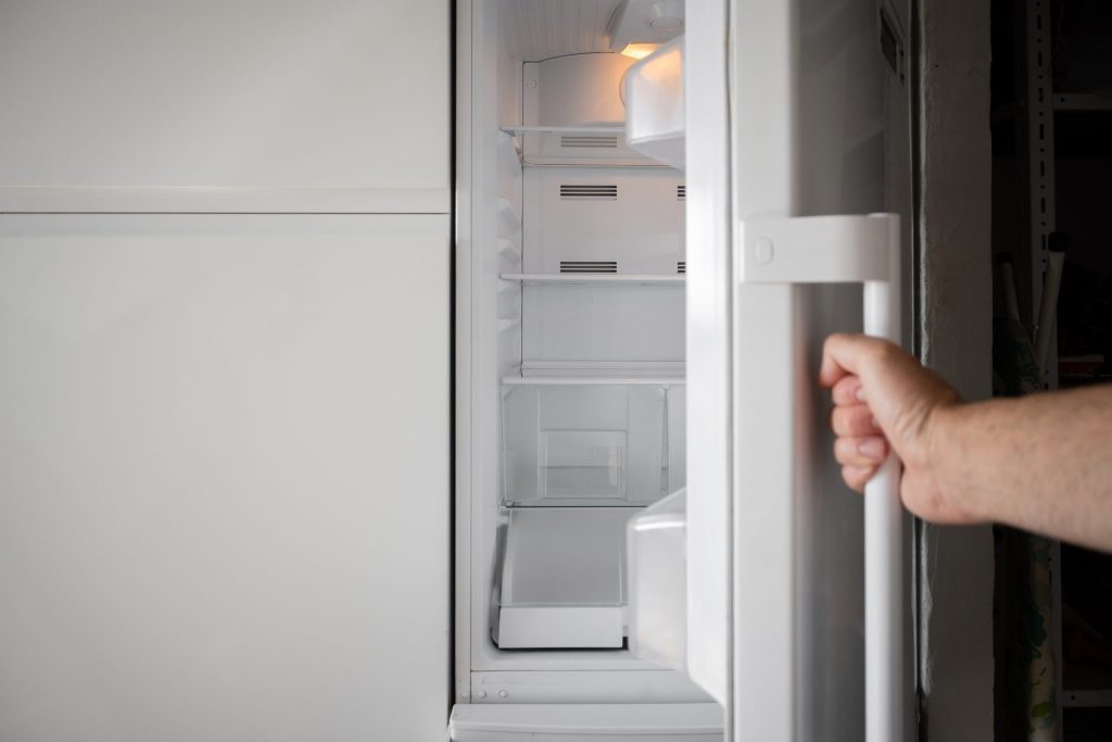 A hand pulling open a refrigerator door, the edge of the door and its seal in view.