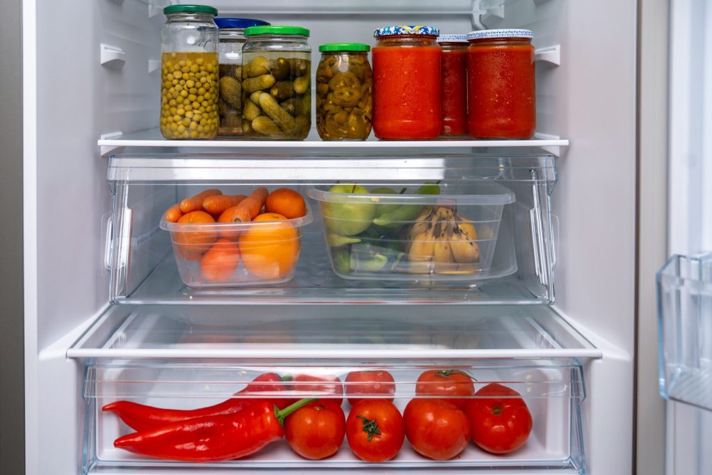 An open refrigerator packed with jars, containers of fruit and vegetables in the crisper.