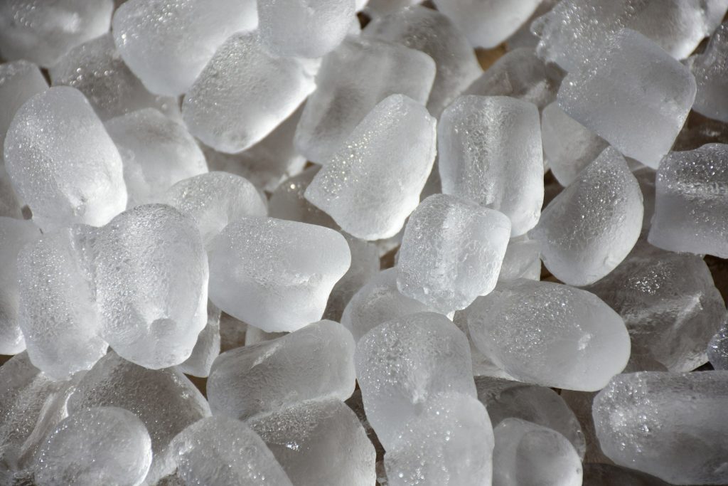 A close heap of machine-made ice cubes, hollow-ended, wet at the edges.