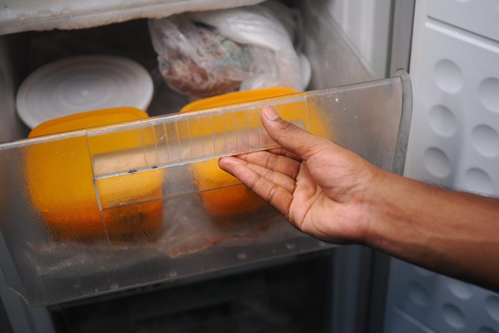 A hand drawing out a frosted freezer drawer, cold vapour lifting off the packets inside
