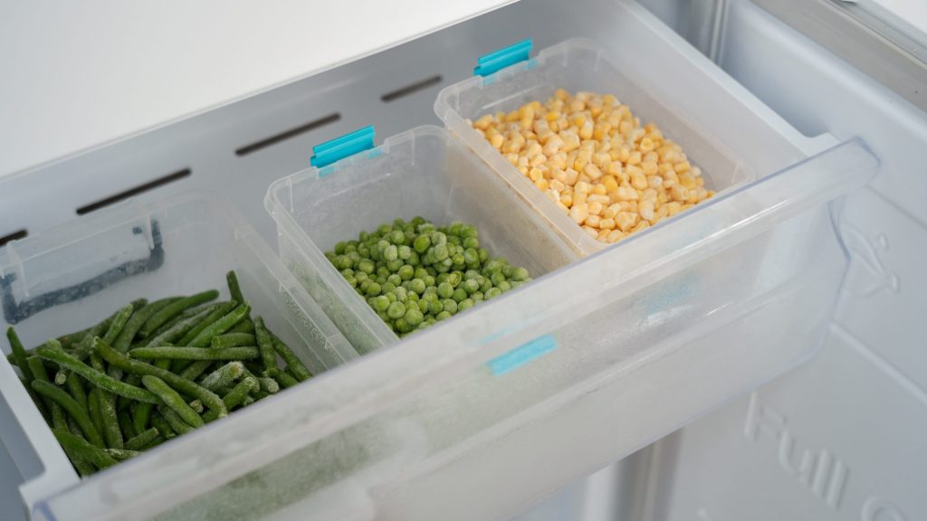 Clear freezer drawers pulled out on stacked containers of frozen beans, peas and corn