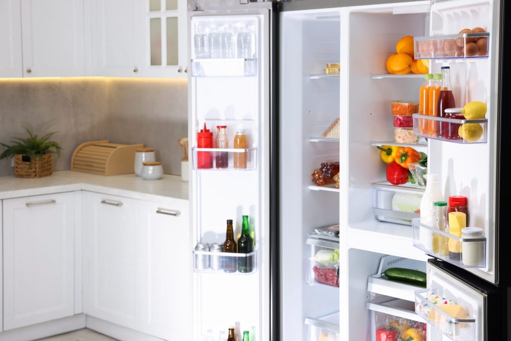 A side-by-side refrigerator with both doors open in a white kitchen, shelves full of food.