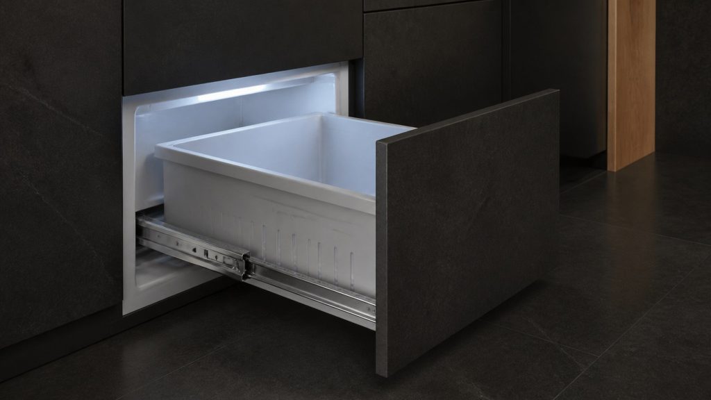A freezer drawer pulled right out to the end of its telescopic runners, the empty basket and the polished rails catching cold light.