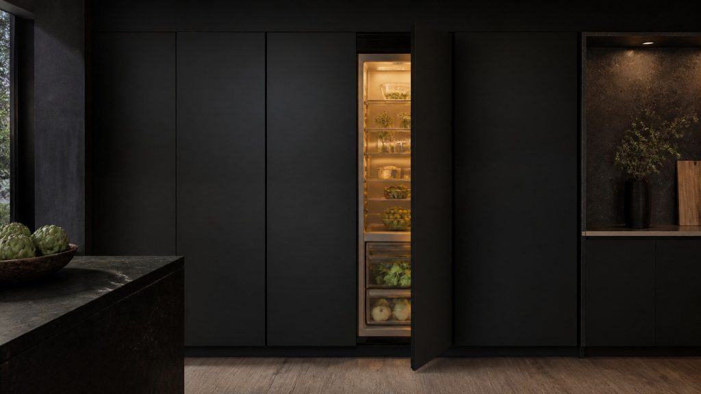 A handleless run of near-black cabinet fronts in a dark kitchen, one tall front slightly open on a lit refrigerator interior behind it.