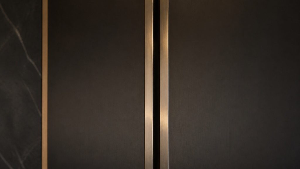 The narrow joint where two refrigeration columns meet in a run, brushed metal edges and a dark shadow line between them, raking amber light.