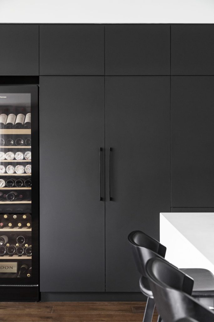 A tall wine cabinet lit from within, set into a run of near-black cabinetry