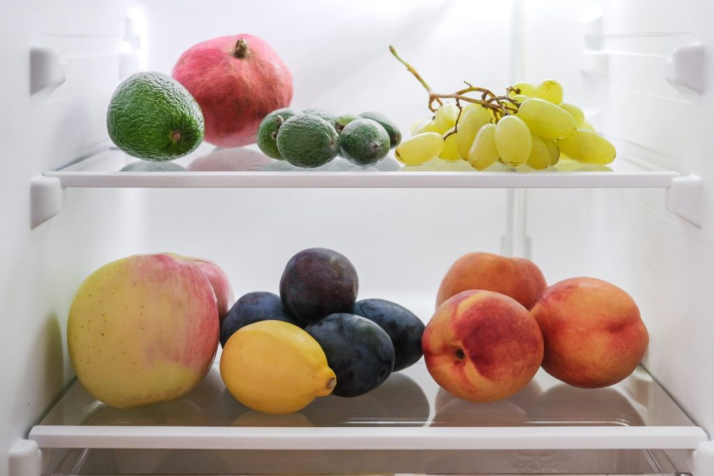 Fruit resting on two glass shelves inside a cold, brightly lit refrigerator