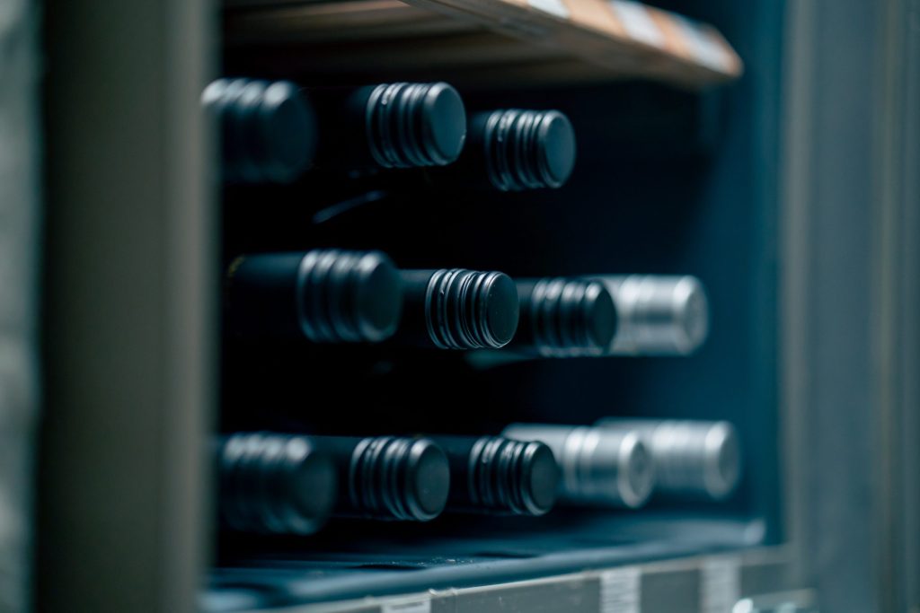 Wine bottles resting on the shelves of a cooled cabinet, seen through its glass door